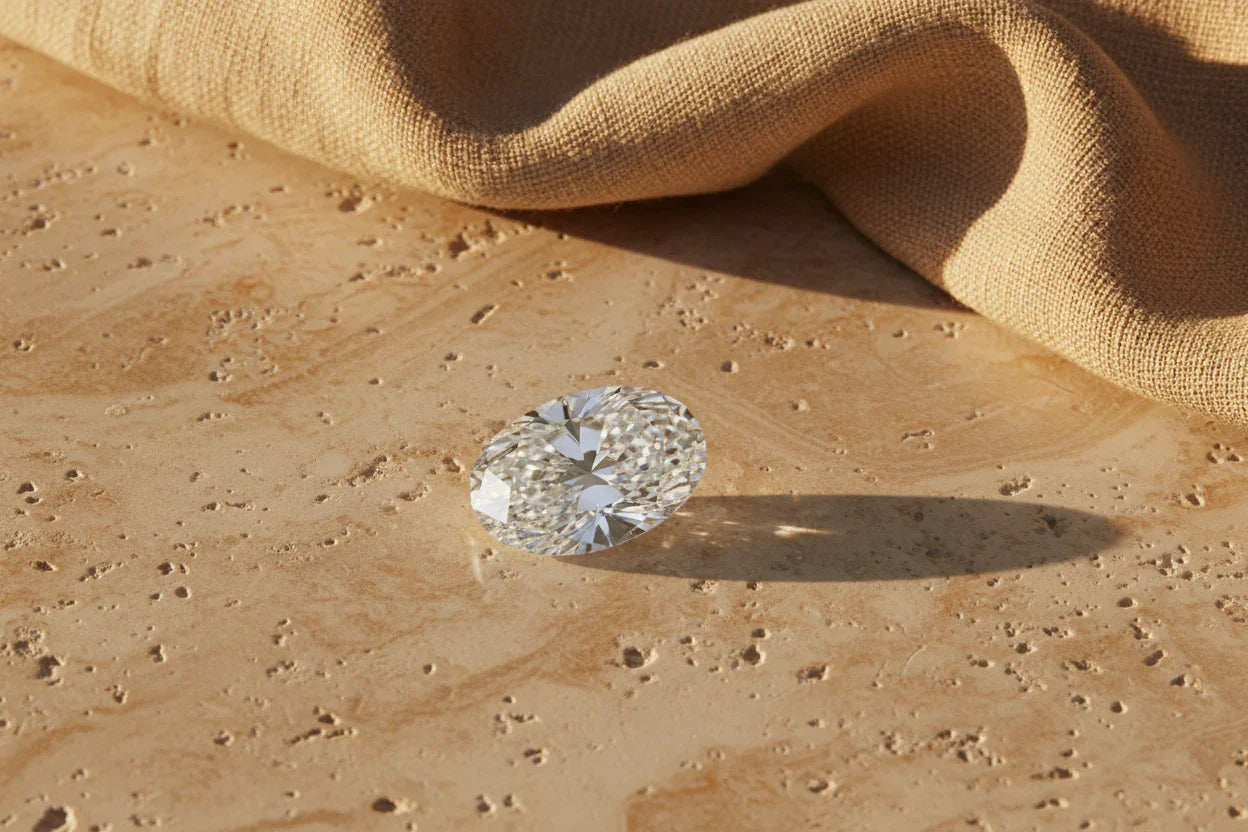 Oval cut loose diamond on textured stone surface with fabric backdrop, ideal for bespoke engagement rings